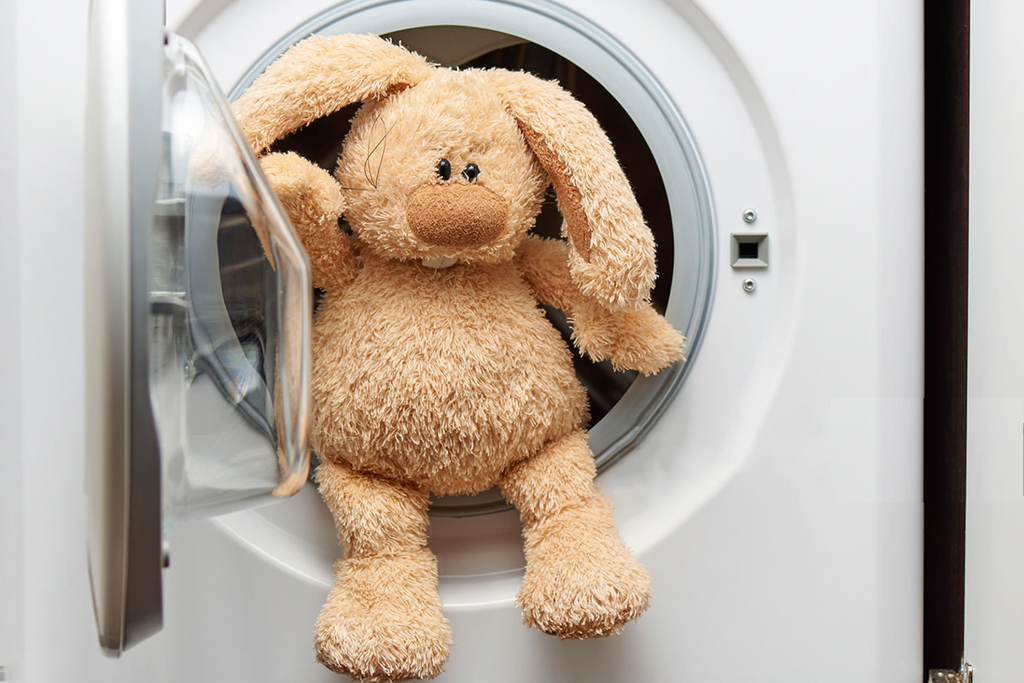 A stuffed animal and bottle of laundry detergent on top of a washing machine.